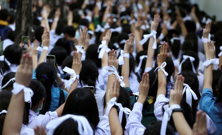 Students wearing white ribbons on their hair and wrists make the three-finger salute to show support for the student-led democracy movement outside the Education Ministry in Bangkok, Thailand. REUTERS/Athit Perawongmetha  